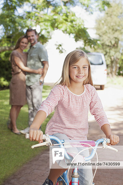 Porträt des lächelnden Mädchens auf dem Fahrrad mit Eltern im Hintergrund