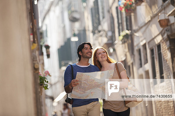 Lächelndes Paar mit Karte auf der schmalen Straße in Venedig