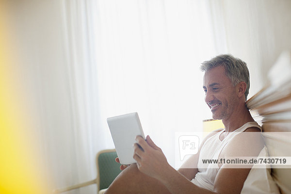 Lächelnder Mann mit digitalem Tablett im Bett