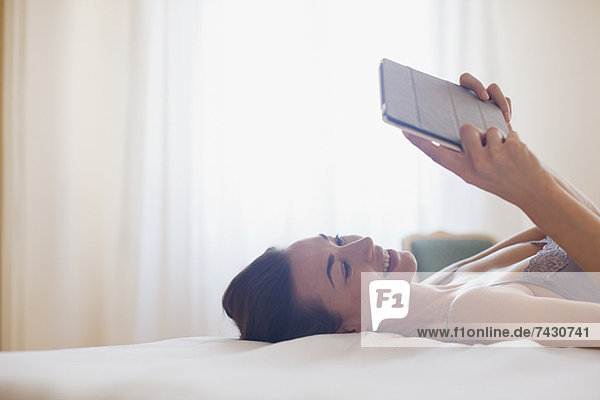 Lächelnde Frau auf dem Bett liegend und mit digitalem Tablett