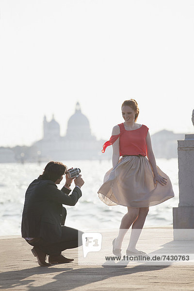 Mann filmt lächelnde Frau am Wasser in Venedig