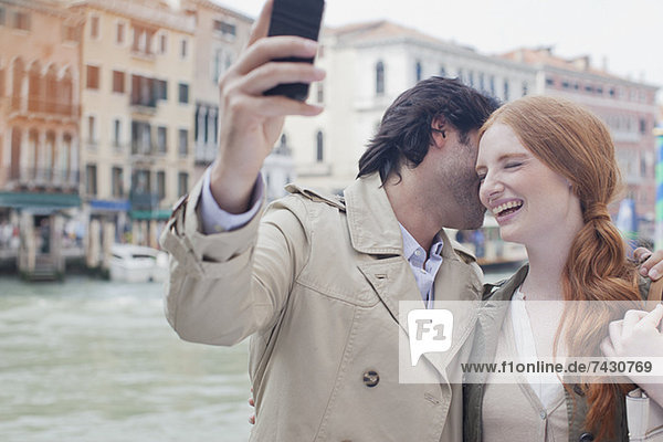 Lachendes Paar beim Selbstporträt mit Fotohandy am Wasser in Venedig