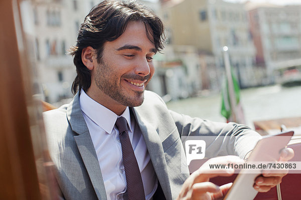 Lächelnder Geschäftsmann mit digitalem Tablett auf dem Schiff in Venedig