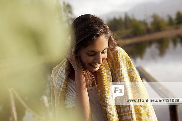 Lächelnde Frau in Decke gehüllt am Seeufer