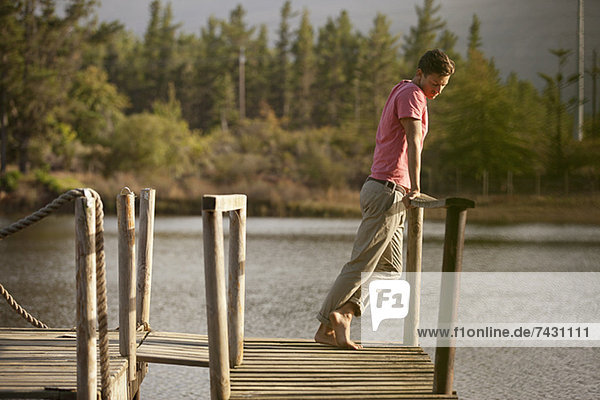 Gelassener Mann steht am Geländer des Docks über dem See