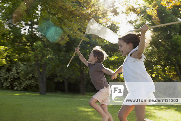 Glückliche Jungen und Mädchen halten sich an den Händen und laufen mit Schmetterlingsnetzen im Gras.