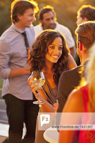 Smiling woman with wine glass talking to man on sunny balcony