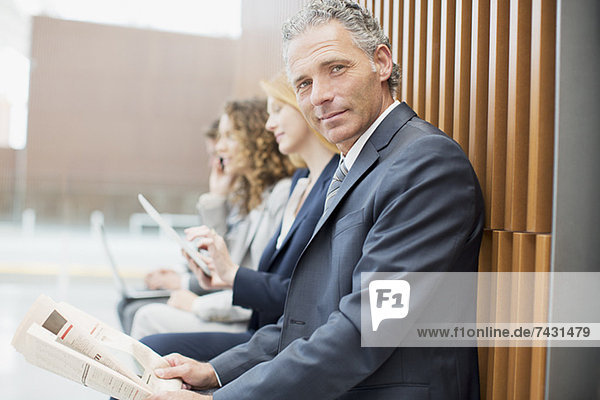 Porträt eines selbstbewussten Geschäftsmannes beim Zeitungslesen mit Mitarbeitern im Hintergrund