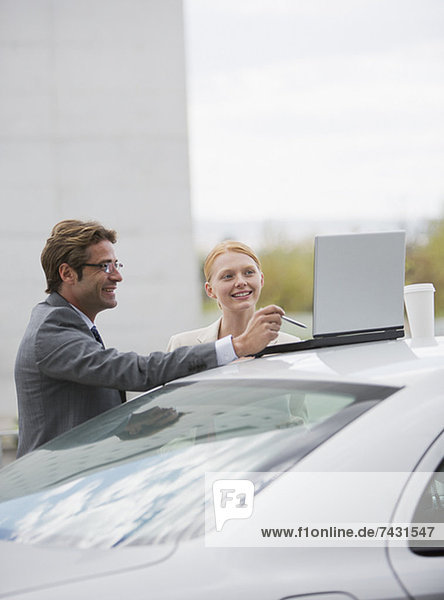 Lächelnder Geschäftsmann und Geschäftsfrau mit Laptop auf dem Auto