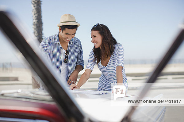 Lächelndes Paar liest Straßenkarte auf Cabriolet