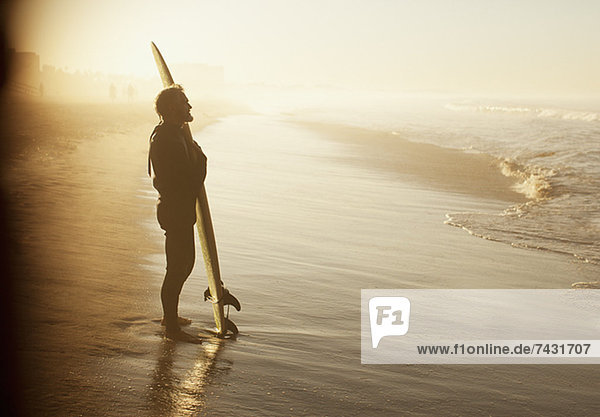 Surfer stehend mit Brett am Strand