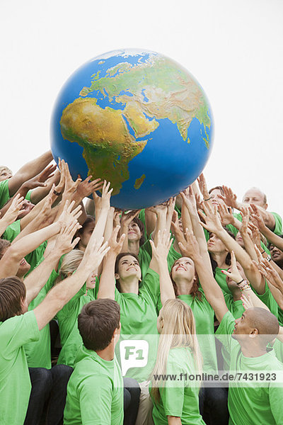 Team in grünen T-Shirts greift nach dem Globus über Kopf