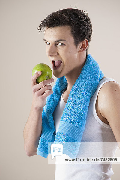 junger lachender Mann beißt in einen Apfel