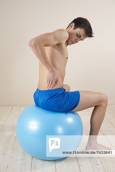 junger Mann betastet seinen Rücken auf einem Gymnastikball