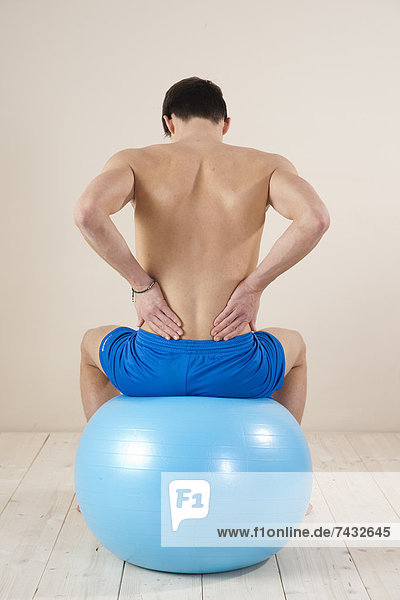 junger Mann dehnt seinen Rücken auf einem Gymnastikball
