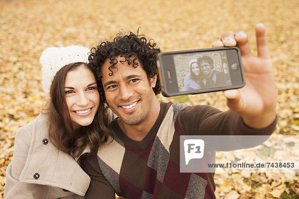 Couple taking picture of themselves in autumn leaves