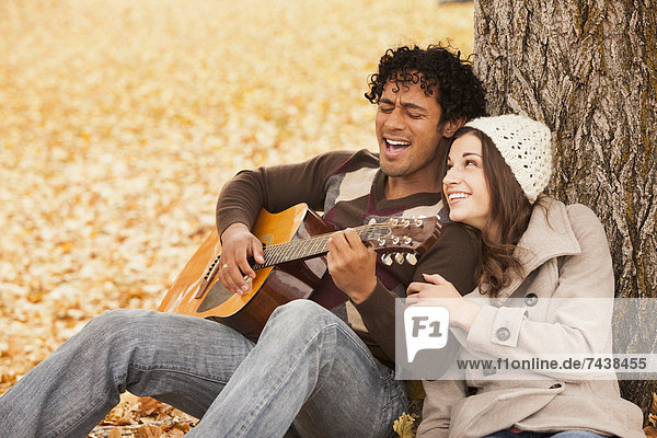 Man playing guitar for girlfriend in autumn leaves