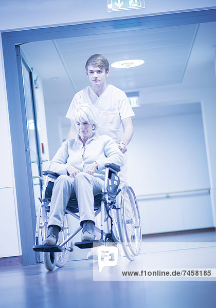 Krankenpfleger schiebt ältere Patientin im Rollstuhl