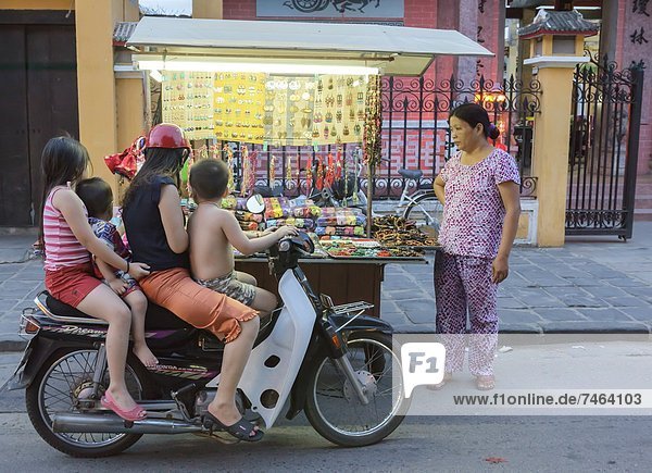 Children stop by on their motorbike to look at trinkets being sold by a woman with a push cart  Hoi An  Vietnam  Indochina  Southeast Asia  Asia