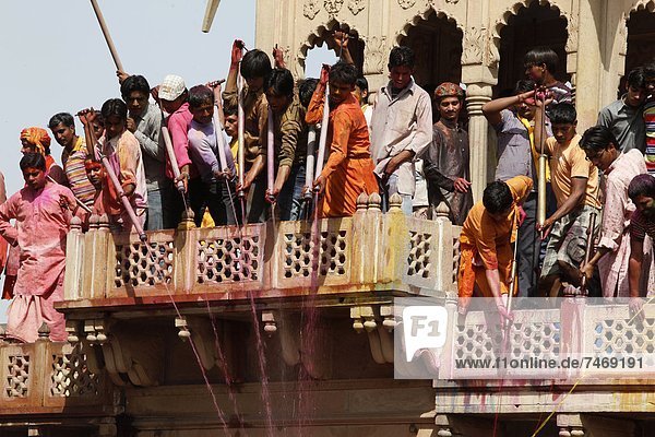 Young men celebrating Holi festival by splashing colored fluids on temple visitors  Nandgaon  Uttar Pradesh  India  Asia