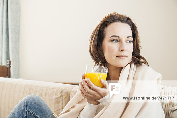 Woman having cup of juice on sofa