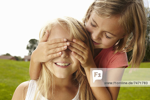 Lächelndes Mädchen bedeckt die Augen der Freunde