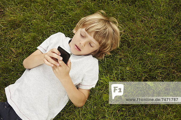 Junge benutzt Handy im Gras