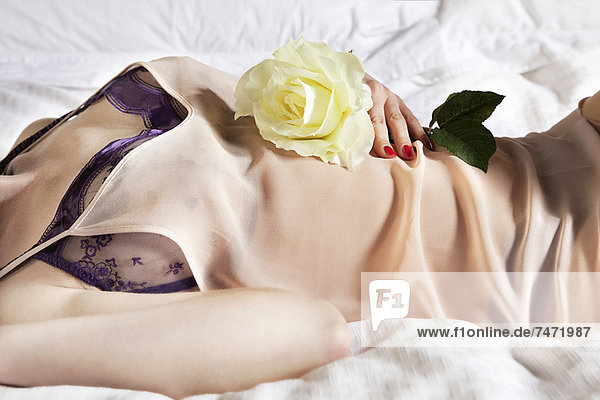 Frau in Dessous mit Blume auf dem Bett