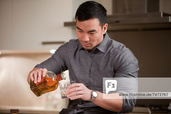 Mann gießt ein Glas Whiskey in die Küche