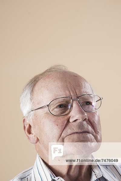 Portrait of Senior Man wearing Aviator Eyeglasses and Looking up into the Distance with Concerned Expression in Studio on Beige Background