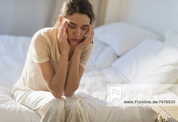 Young woman sitting on bed with headache