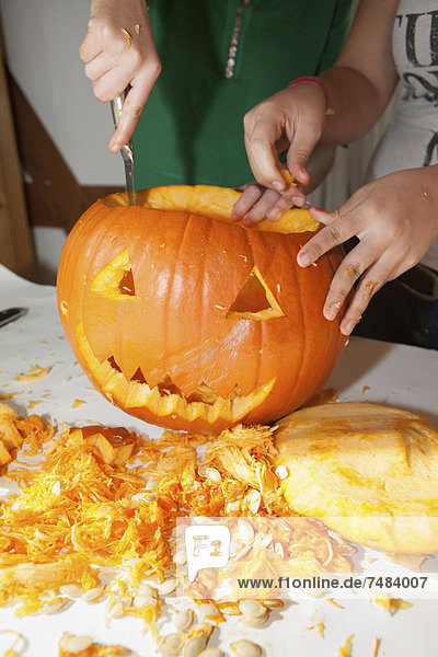 Zwei Mädchen  etwa 14 Jahre  schneiden ein Gesicht in einen Halloween-Kürbis