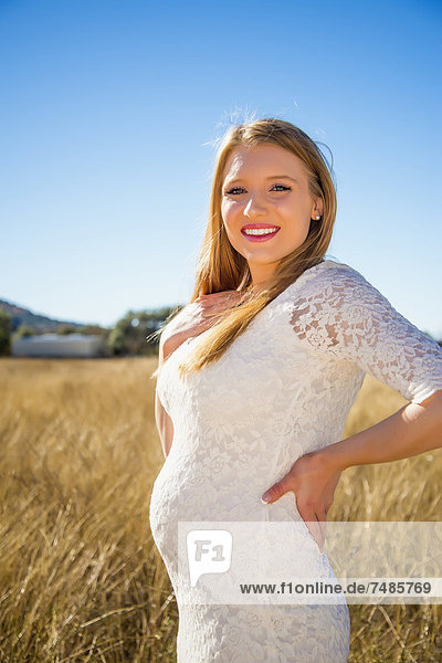 USA  Texas  Schwangere junge Frau im Gras stehend  lächelnd  Portrait