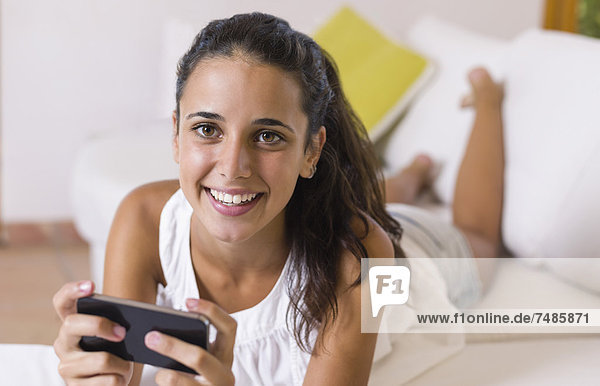Teenage girl lying on white couch and using smart phone  smiling  portrait