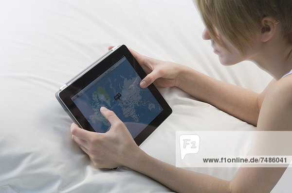 Germany  Young woman using digital tablet while lying on bed