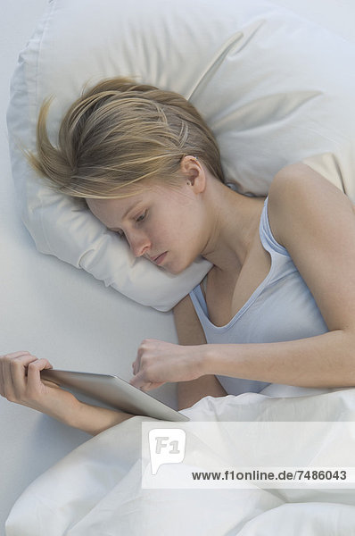 Germany  Young woman using digital tablet while lying on bed