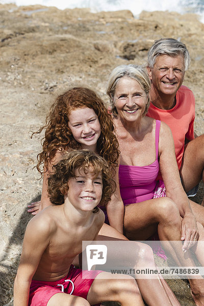 Spanien  Großeltern mit Enkelkindern am Strand sitzend  lächelnd  Portrait