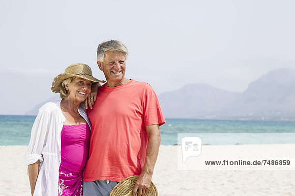Spanien  Seniorenpaar am Strand stehend  lächelnd
