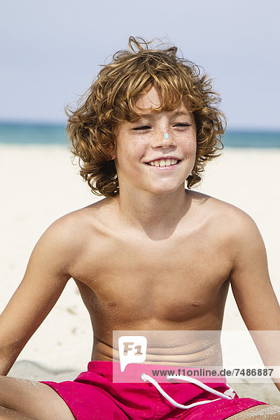Spain  Boy sitting on beach  smiling