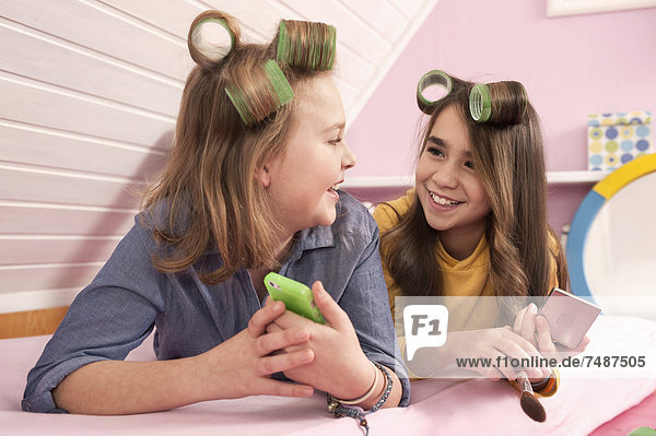 Mädchen mit Haarrollen liegend und beobachtend Smartphone  lächelnd