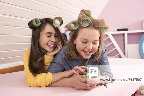 Mädchen mit Haarrollen liegend und beobachtend Smartphone  lächelnd