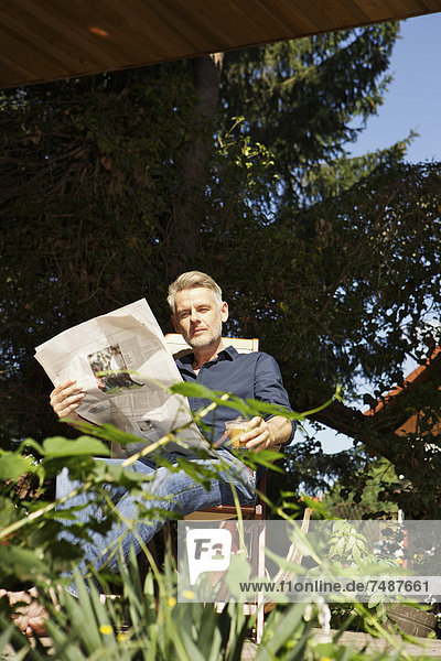 Mature man sitting on terrace and reading newspaper