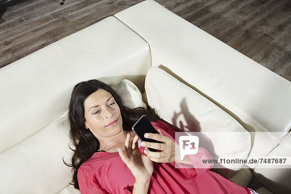Mature woman lying on sofa and using mobile phone
