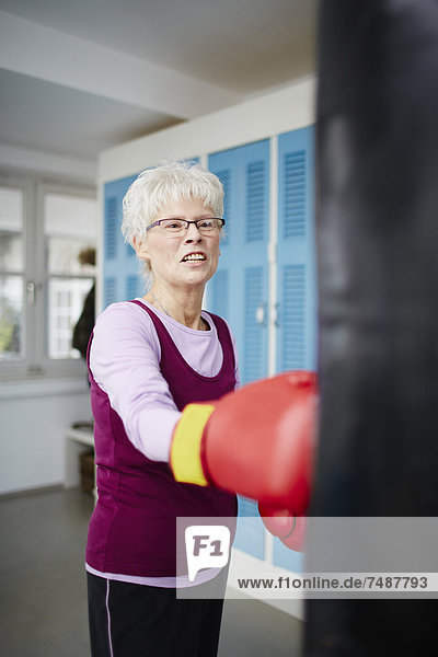 Senior woman with boxing glove and punch bag