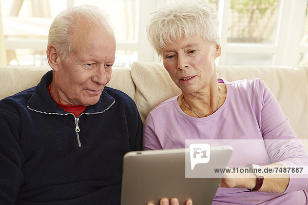 Deutschland  Düsseldorf  Seniorenpaar mit digitalem Tablett und Entspannung zu Hause