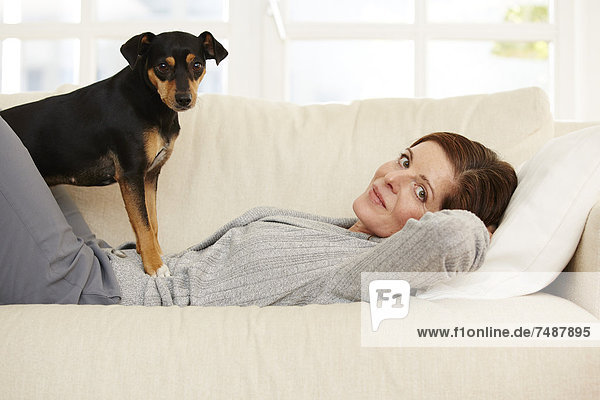 Reife Frau auf dem Sofa liegend mit Hund