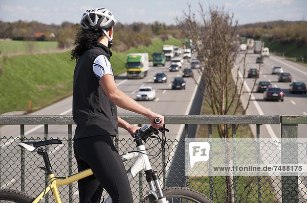 Germany  Mid adult woman with mountain bike on bridge looking at traffic on highway