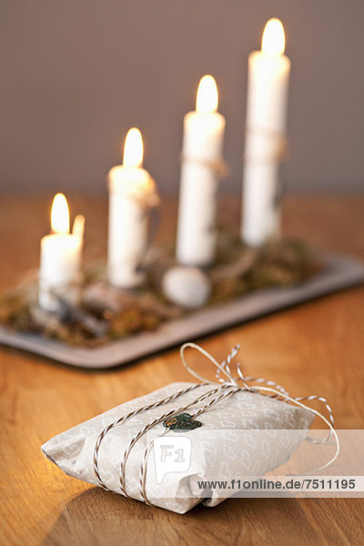 Versiegeltes Geschenk mit angezündeten Kerzen auf Holztisch