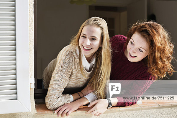 Cheerful young female friends looking through house window