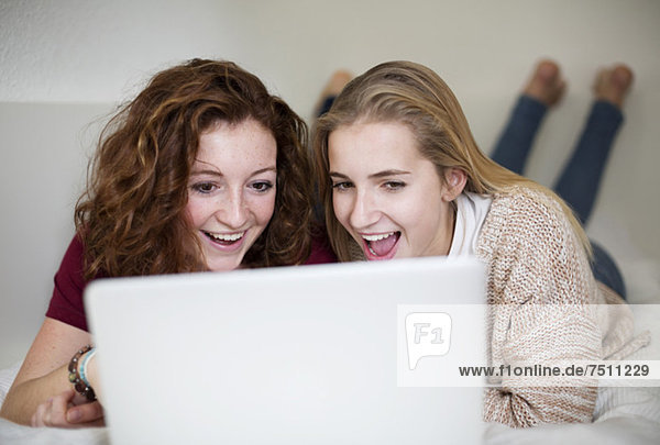 Überraschte junge Mädchen  die im Bett liegend den Laptop benutzen.